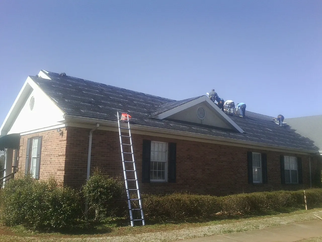 Crew tearing shingles off a brick ranch roof with a ladder set — Emergency Roof Repair work by our crew in Yarmouth