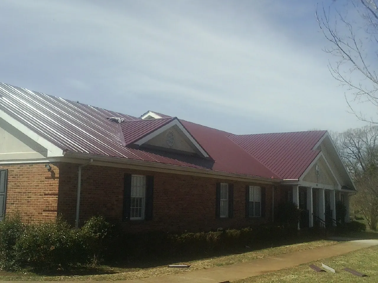 Red metal roof with gabled entries on a long brick building, from a Hail Damage Roof Repair job in Yarmouth