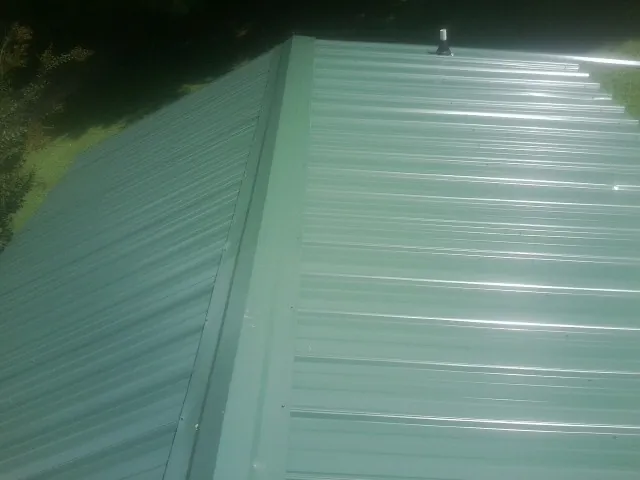 New green metal panels meeting at the ridge of a roof — Flat Roof Repair work by our crew in Yarmouth