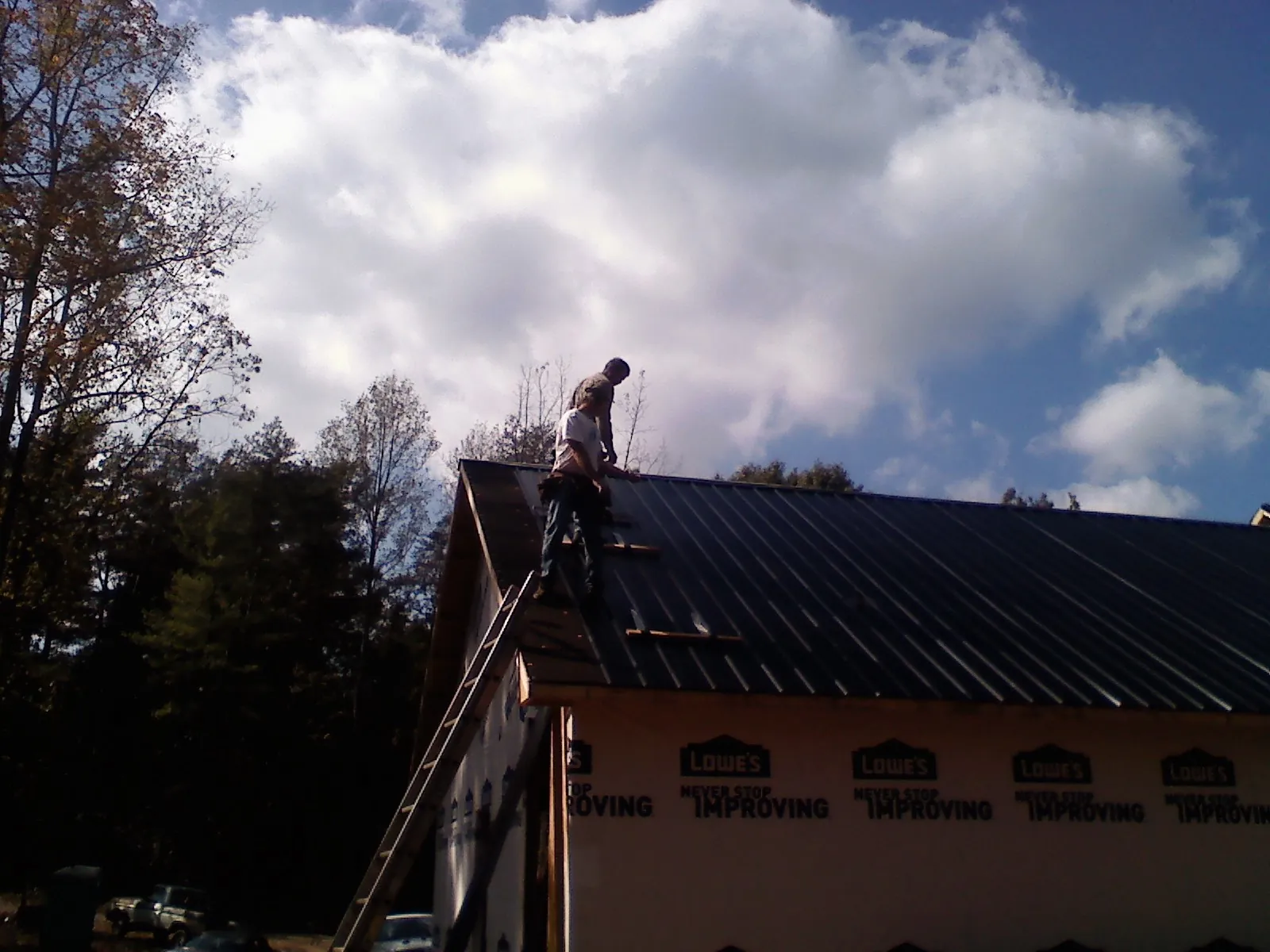 Roofer fastening dark metal panels high against a cloudy sky, from a Roof Inspection job in Yarmouth