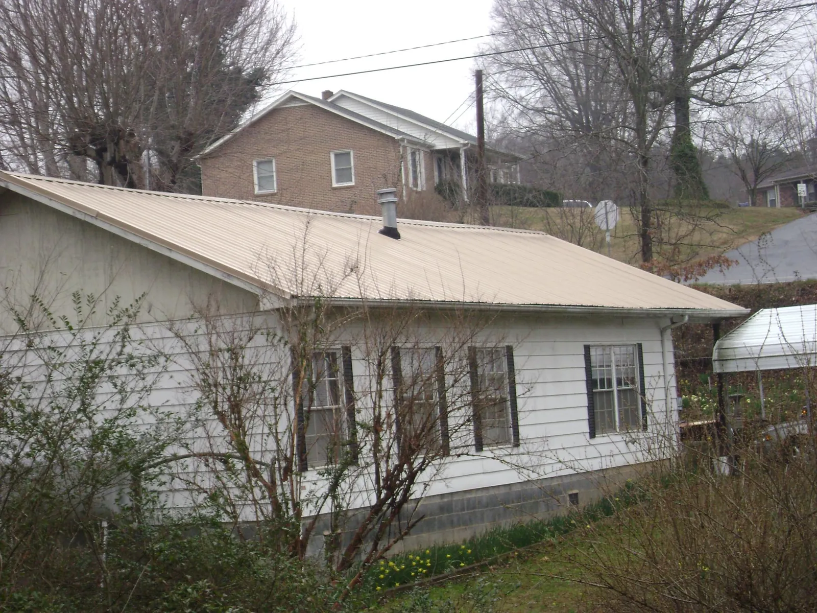 Tan metal roof on a white sided house set into a hillside — Commercial Roofing by Roofing Brothers in Yarmouth